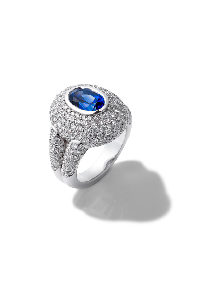 A silver pavé ring featuring a large oval-cut blue sapphire center stone, photographed on a clean white background with a soft shadow.